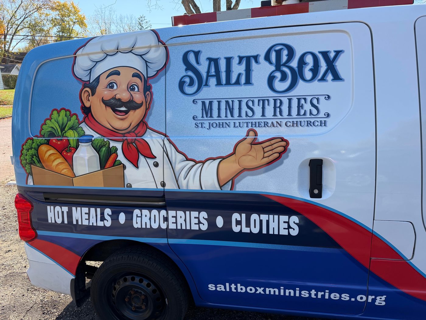 The Saltbox Ministries van, a white, navy and red Nissan NV200 with the chef logo on its side